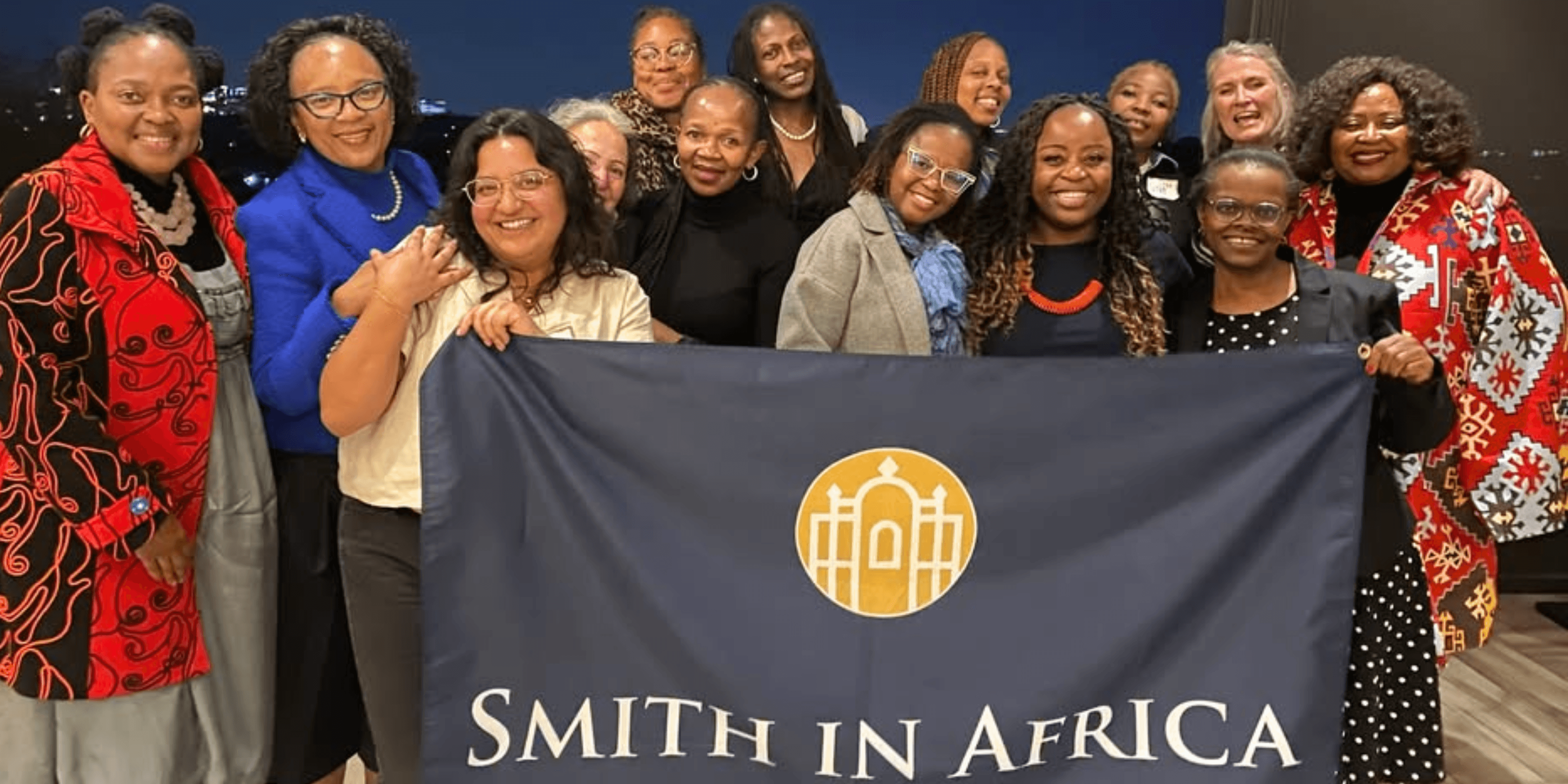 Diverse group of women smiling behind a navy blue banner reading 'SMITH IN AFRICA'.