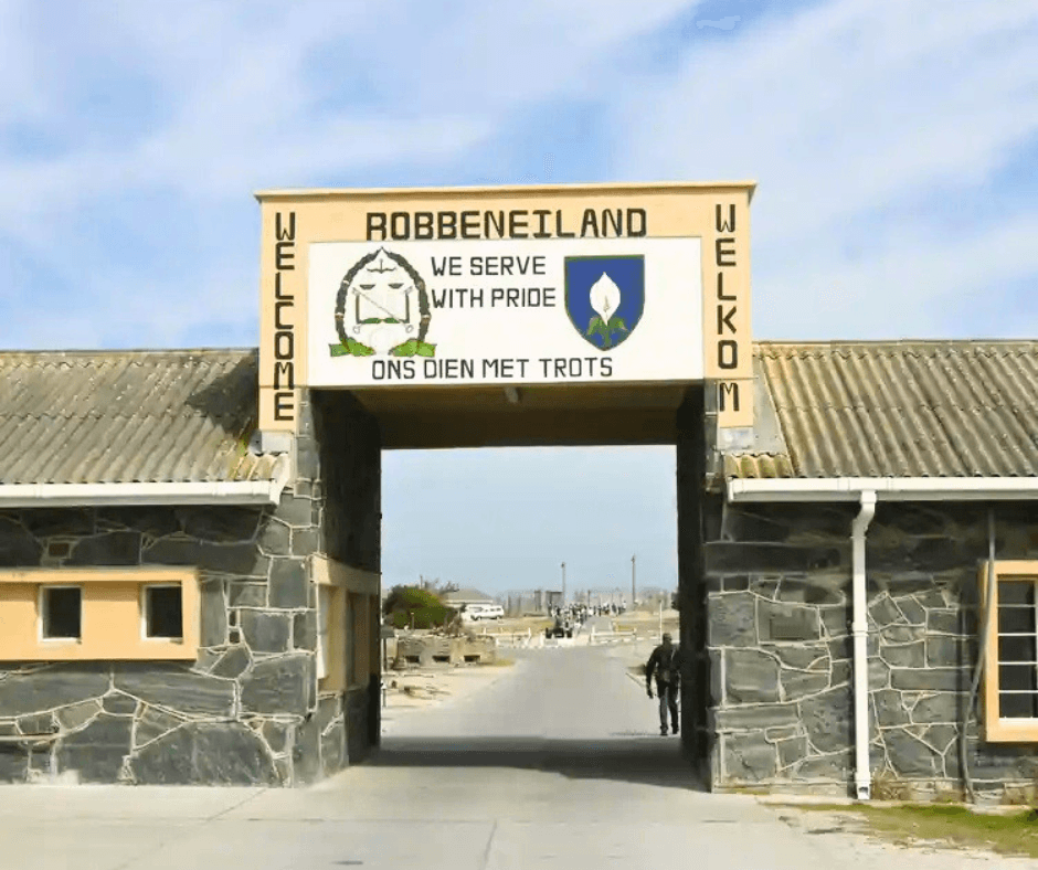 Stone entrance gate to Robben Island with bilingual signs under a bright sky.