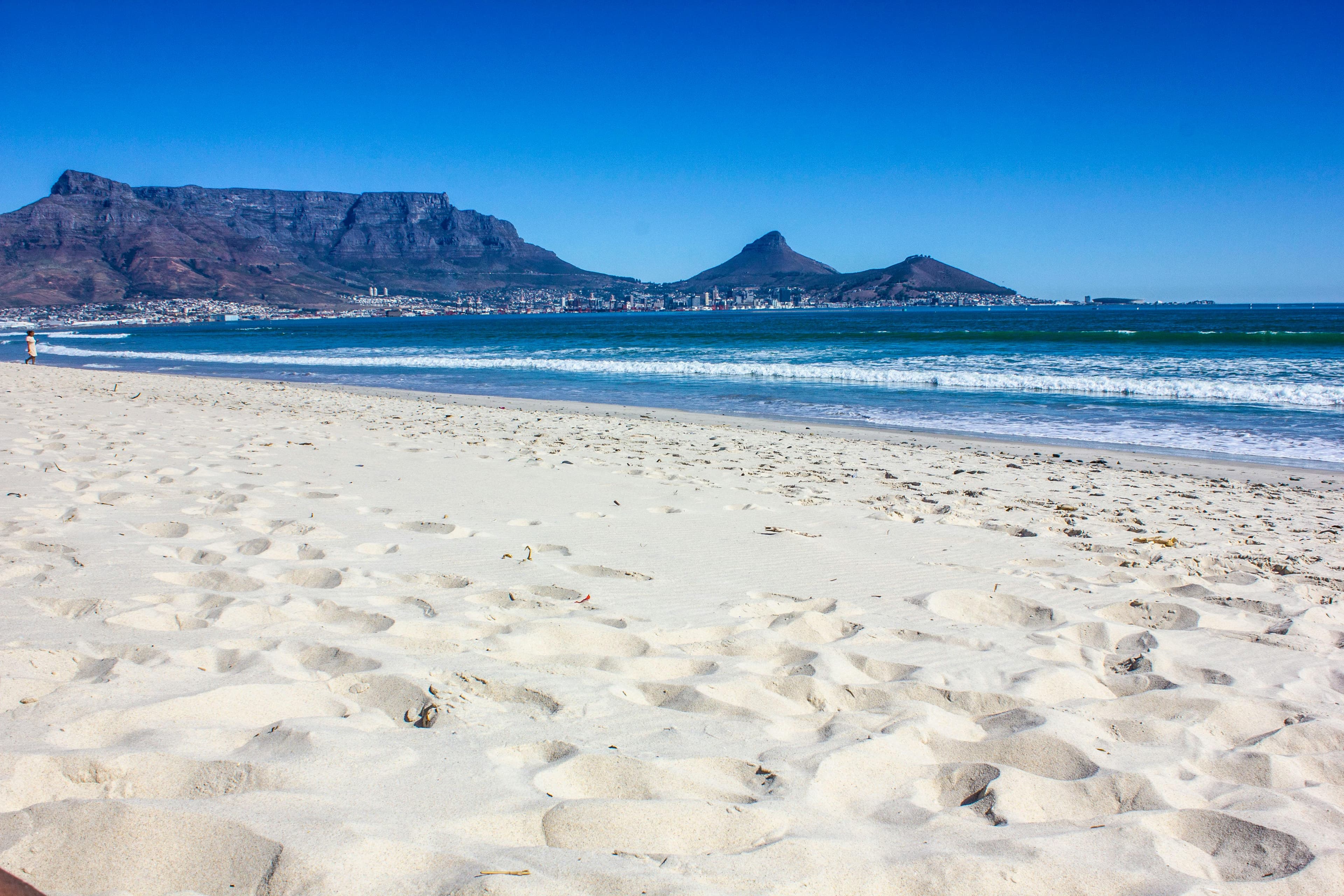 White sandy beach and blue waves with Table Mountain and Lion's Head in Cape Town.