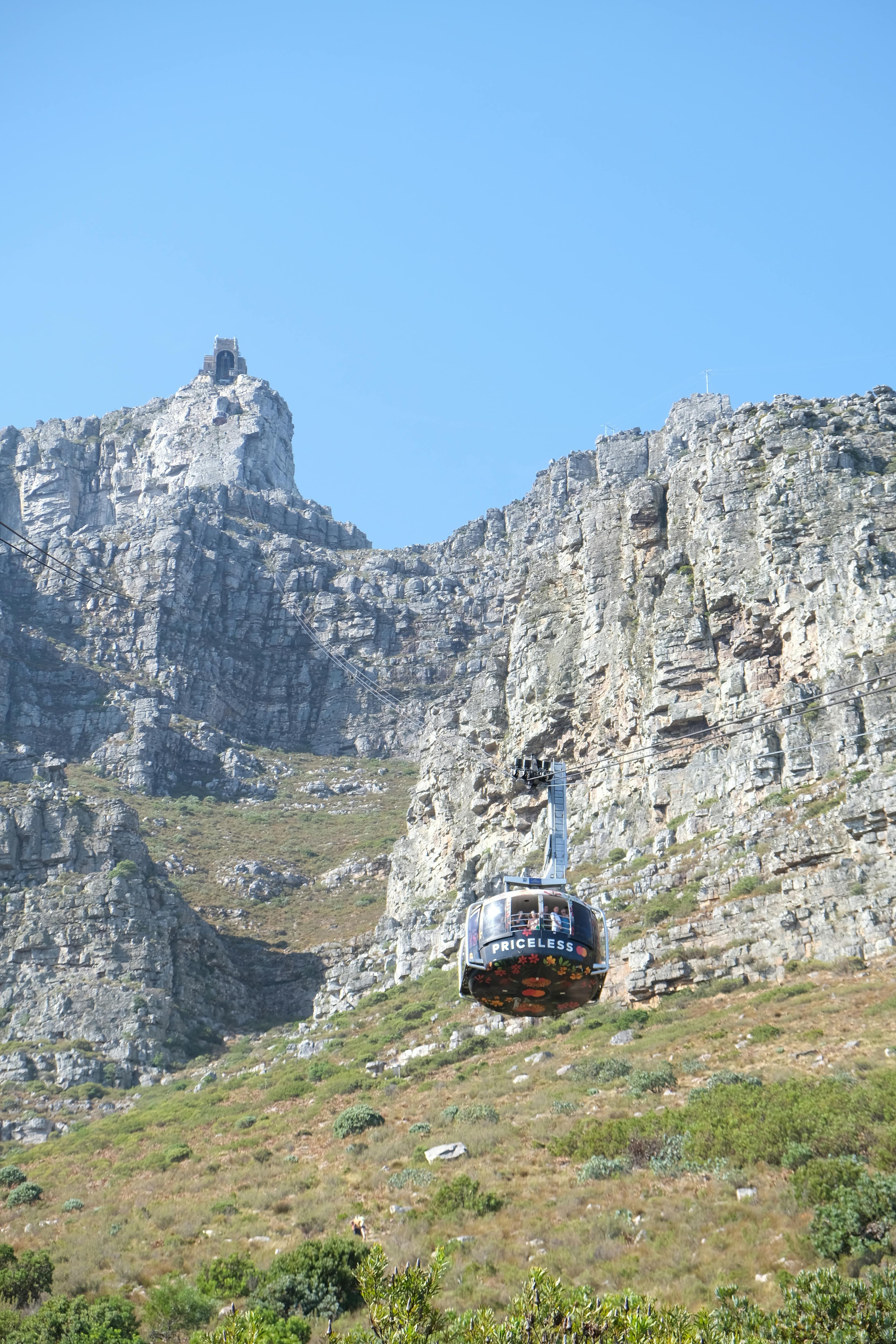 Cable car ascends the steep rocky cliffs of Table Mountain against a blue sky.